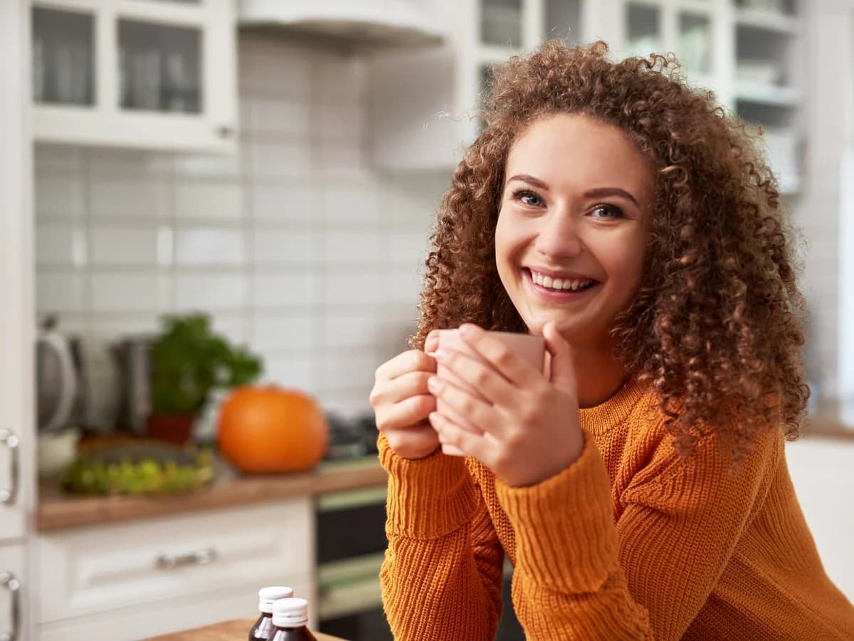 Vrouw met een kop thee in een lichte keuken.